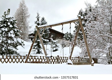 A Snow-covered Wooden Swingset In An Alpine Winter Setting.