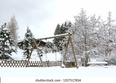 A Snow-covered Wooden Swingset In An Alpine Winter Setting.