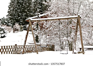 A snow-covered wooden swingset in an alpine winter setting.