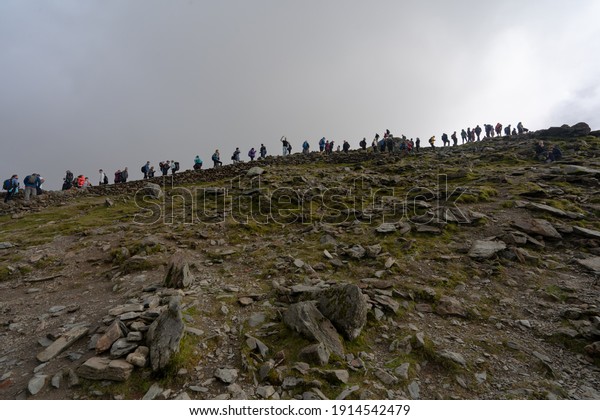 SNOWDONIA, UK - 2020: A long queue of\
people social distancing on Snowdon mountain in\
Wales