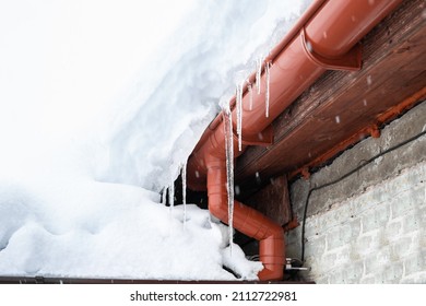 A snowdrift on the roof of a house from which icicles hang. Cleaning roofs from accumulated snow.