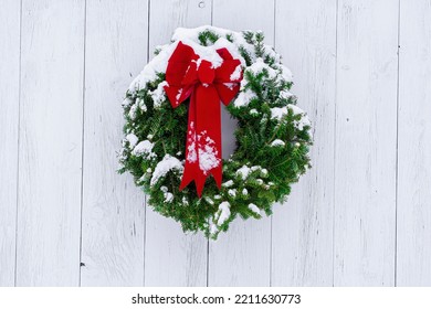 Snow-dusted pine needle Christmas wreath and red bow on weathered, whitewashed wide plank door. Rustic, rural, natural, traditional country Christmas.  - Powered by Shutterstock