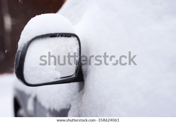 Snowed car. Rear view mirror at selective focus.\
Shallow depth of field.