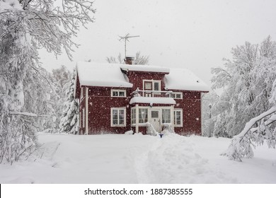 Snowfall in the village. Blurred background. Old wooden house in the snow. Traditional typical Scandinavian Swedish house or villa in the countryside in winter. Red cottage under snow flakes.