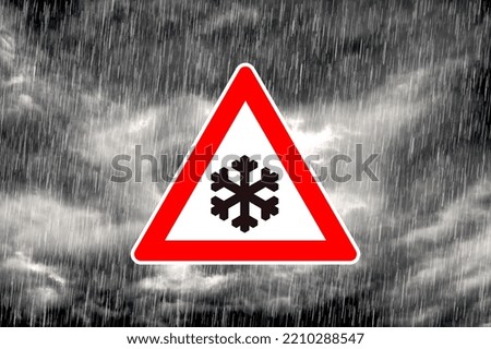 Snowfall warning sign in front of dramatic gray cloudy sky with precipitation