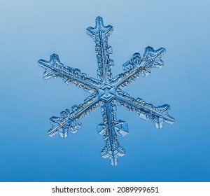 Snowflake on smooth gradient background. Macro photo of real snow crystal on glass surface. This is small snowflake with unusual pattern.
