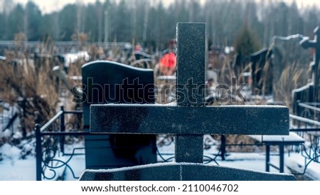 Snowing in the public cemetery. Traditional graveyard in winter under snow. Tombstone on the necropolis. Cemetery covered by snow in winter. Dramatic sky background. Space for text.