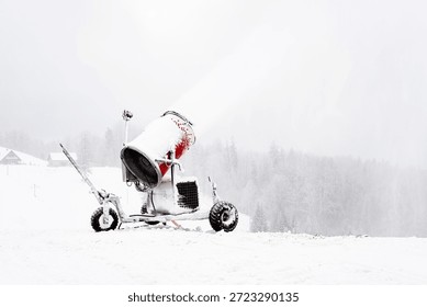 Snowmaking machine operating in winter cold, spraying artificial snow on ski slope amid fog, silence and isolation in Nordic landscape.