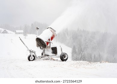 Snowmaking machine operating in winter cold, spraying artificial snow on ski slope amid fog, silence and isolation in Nordic landscape.