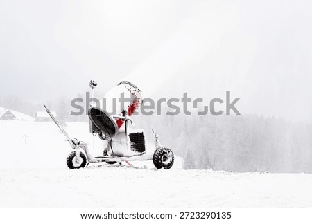 Snowmaking machine operating in winter cold, spraying artificial snow on ski slope amid fog, silence and isolation in Nordic landscape.