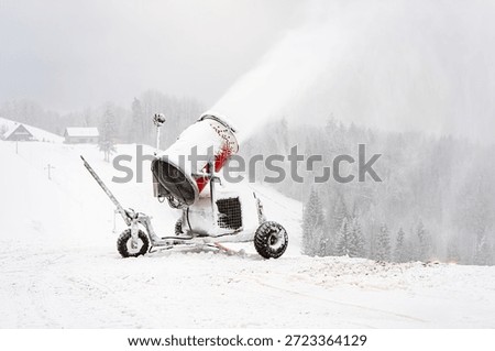 Snowmaking machine operating in winter cold, spraying artificial snow on ski slope amid fog, silence and isolation in Nordic landscape.
