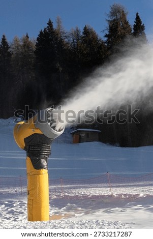 Snowmaking machine producing artificial snow on a ski slope in winter. Modern snow cannon working at a mountain ski resort, preparation of pistes for winter sports and tourism.