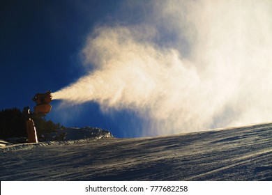Snowmaking on slope. Skier near a snow cannon making fresch powder snow. Mountain ski resort and winter calm mountain landscape.  