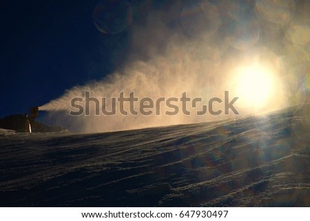 Snowmaking on slope. Skier near a snow cannon making fresh powder snow. Mountain ski resort and winter calm mountain landscape.   Winter specific