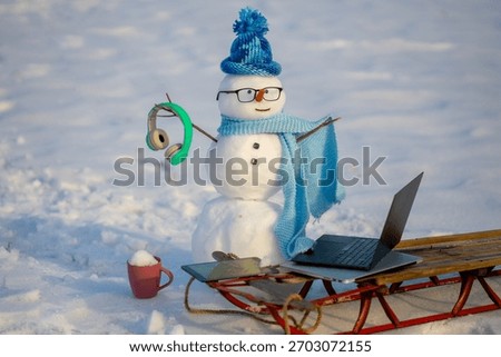 Snowman programmer. Snowman browsing internet in snowy field. Winter business. Snowman doing remote work in winter landscape. Snowman with laptop and sled outdoors.