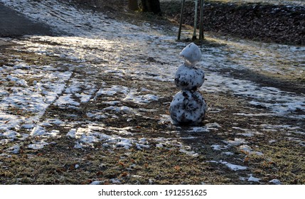 A Snowman Sadly Slowly Melting, Dirty From Mud And Lack Of Snow Will Evoke A Feeling Of Ruin And Ugly Changeable Weather Of Winter February. Frozen Snow On Lawn