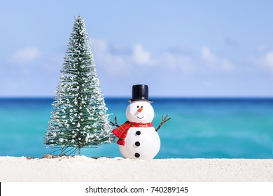 Snowman Toy And Fir Tree At White Sandy Beach On Caribbean Sea Background. Christmas Celebration
