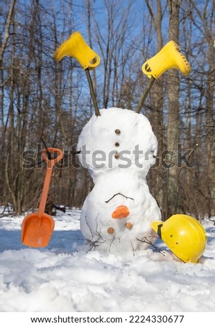 snowman in yellow boots with shovel, construction helmet turned upside down in snowy forest. winter fun, joyful seasonal games for children. idea of christmas greetings in construction companies