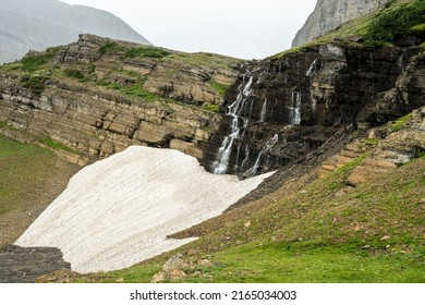 Snowmelt Drops Over Cliff Wall And Under Snow Field Along The Piegan Pass Trail In Glacier National Park