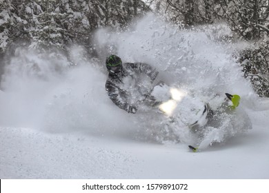 Snowmobile Rider Makes A Turn And Jump During A Snowfall. In The Winter Forest, Leaving Behind A Trail Of Big Splashes Of White Snow From A Snow Bike. Bright Snowmobile And Black Suit. Snowmobilers