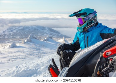 a snowmobiler is resting on top of a mountain, tipping the snowmobile on its side. snowmobile close-up with a sitting rider over the valley - Shutterstock ID 2094110398