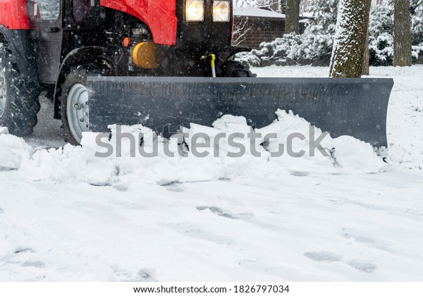 Snowplow removes snow from the sidewalk during a\
snowfall in the park