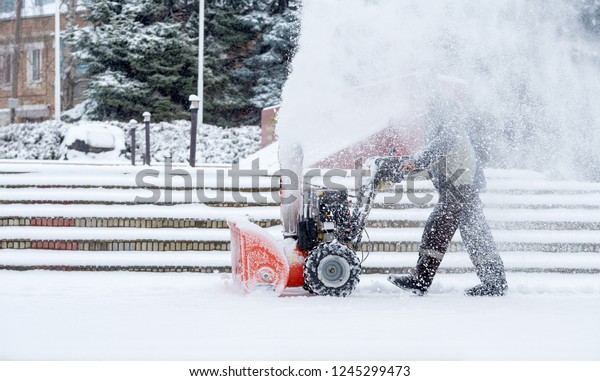 Snow-removal work with a snow blower. Man\
Removing Snow. heavy precipitation and snow\
piles