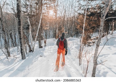 Snowshoeing people in winter forest with snow covered trees on snowy day. Man on hike in snow hiking in snowshoes living healthy active outdoor lifestyle.