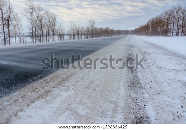 Snowstorm on the highway. Patterns on the winter\
highway in the form of four straight lines. Snowy road on the\
background of snow-covered forest.\
