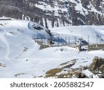 Snowy alpine scene near Zermatt, Switzerland, featuring Gornergrat Railway station, red train on tracks, rugged mountains, and scattered skiers.