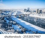 A snowy city with a river running through it. The river is frozen and the bridge is covered in snow. The city is quiet and peaceful, with the snow covering everything