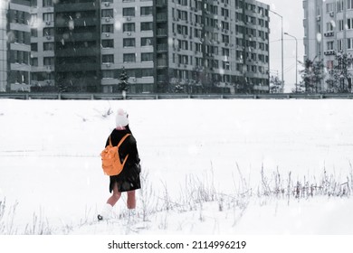 Snowy City Scene. Young Woman With Orange Backpack Walking Alone Urban Street Under Snowfall.