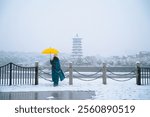 Snowy Day Scene with a Bright Yellow Umbrella in Front of a Pagoda by the Waterfront.