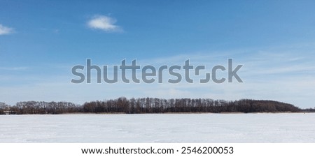 A snowy field with a few trees in the background. The sky is clear and blue