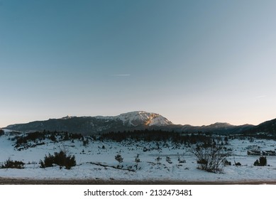 A Snowy Field With Mountains In The Background During Sunset