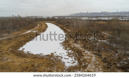 Snowy field with a path through it. The snow is deep and the ground is covered in brown grass. The sky is cloudy. Frozen channels of the great Russian Volga River, near the city of Nizhny Novgorod.