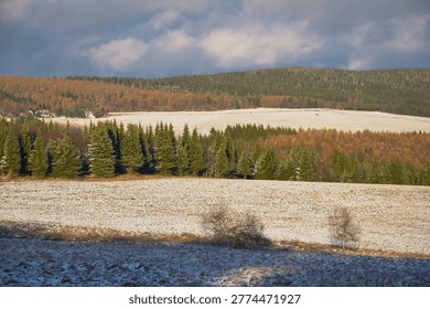 Snowy fields and forest under dramatic winter clouds in the Ore Mountains