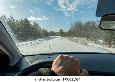 Snowy forest road during snowfall and strong wind. View of the road through the windshield of the car. Car interior defocus