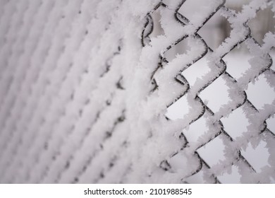 Snowy frozen metal fence close-up.Winter snowy weather.Old rural fence with smaller holes covered with snow.Cloudy cold day.Winter freezing scenery,low temperature