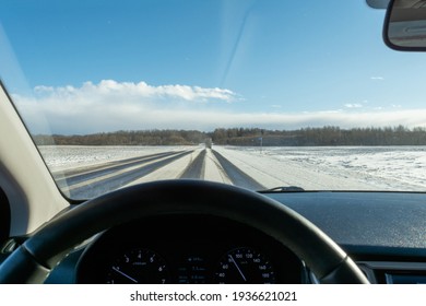 Snowy highway during snowfall and strong wind. Truck goes on winter road. View of the road through the windshield of the car. Sunny day in early spring. Car interior defocus
