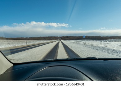 Snowy Highway During Snowfall And Strong Wind. Truck Goes On Winter Road. View Of The Road Through The Windshield Of The Car. Sunny Day In Early Spring. Car Interior Defocus