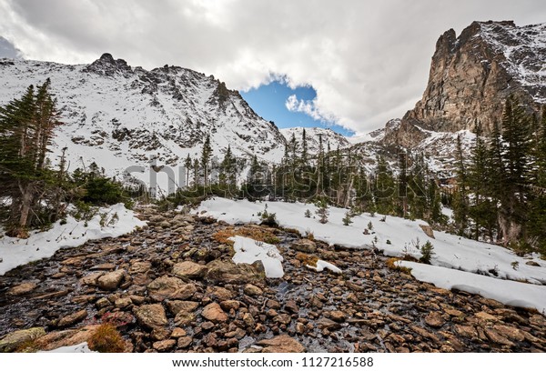 Snowy landscape with rocks and mountains in snow around\
at autumn with cloudy sky. Rocky Mountain National Park in\
Colorado, USA. 