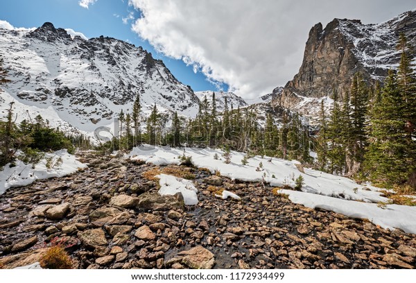 Snowy landscape with rocks and mountains in snow around\
at autumn with cloudy sky. Rocky Mountain National Park in\
Colorado, USA. 