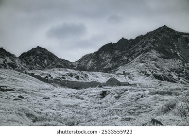 A snowy mountain landscape with a rustic cabin nestled among the slopes under a cloudy sky. - Powered by Shutterstock