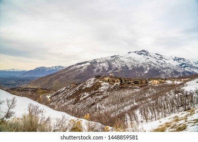 Snowy mountain with leafless trees multi storey homes and road viewed in winter