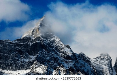 Snowy mountain peak with mist, rugged rocks, and bright blue sky. - Powered by Shutterstock