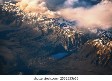 Snowy mountain peaks reach into pink-tinted clouds, with a blue lake nestled in the rugged terrain below. - Powered by Shutterstock