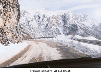 A snowy mountain road winding along rocky cliffs with a guardrail, surrounded by majestic peaks under a clear sky. A winter driving scene showcasing nature's rugged beauty. - Powered by Shutterstock