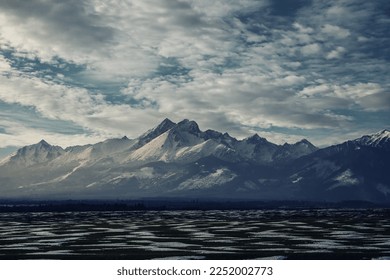 Snowy mountains in the distance. Dramatic view on winter landscape with mountains and rock, covered with snow. Heavy clouds above ski resort - Shutterstock ID 2252002773