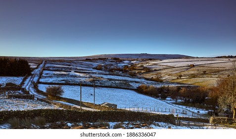 Snowy Nidderdale and late afternoon sun lights up moorland pastures, fields and a single track road